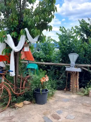 Decoración vintage eventos el regajo Terraza exterior de finca El Regajo con bicicleta vintage oxidada junto a árbol decorado con telas blancas y naranjas, báscula antigua, mesa de piedra circular y vistas panorámicas al valle y montañas al fondo.